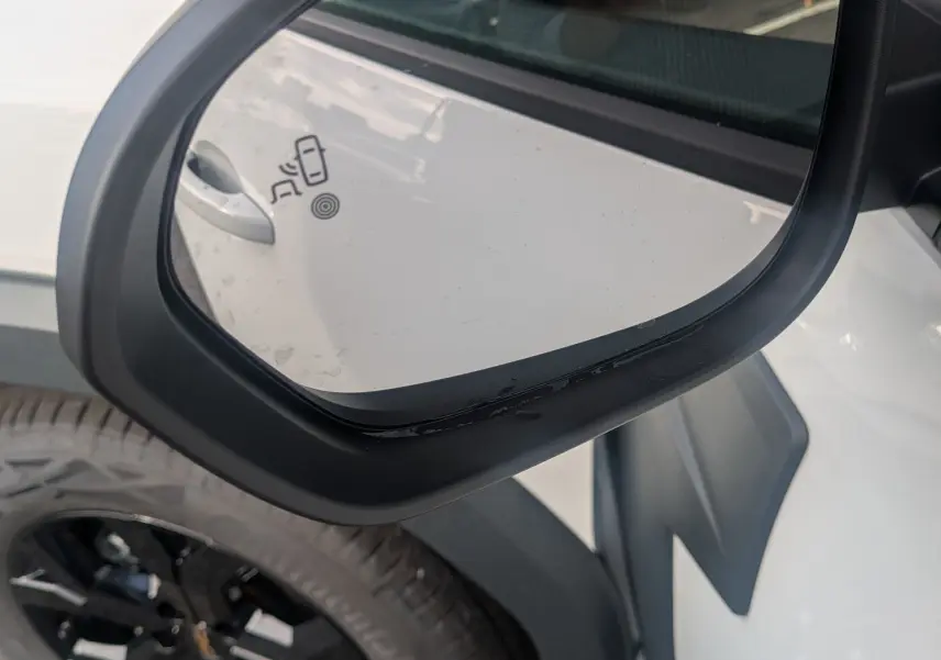 Rétroviseur côté gauche d’un Dacia Duster Hybrid 155 Extreme blanc glacier, avec jante noire et coques brun cuivré.