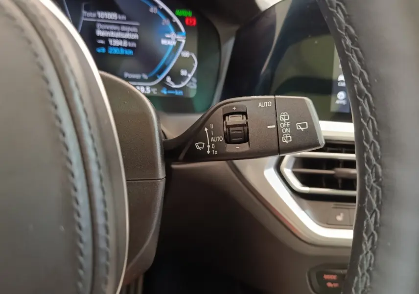 Gros plan sur la commande d’essuie-glace à gauche du volant dans l’habitacle d’une BMW Série 3 gris foncé 320e hybride.