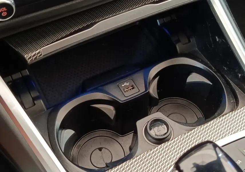 Gros plan sur les porte-gobelets et prise USB du coffre central d’une BMW Série 3 320e gris foncé hybride rechargeable.