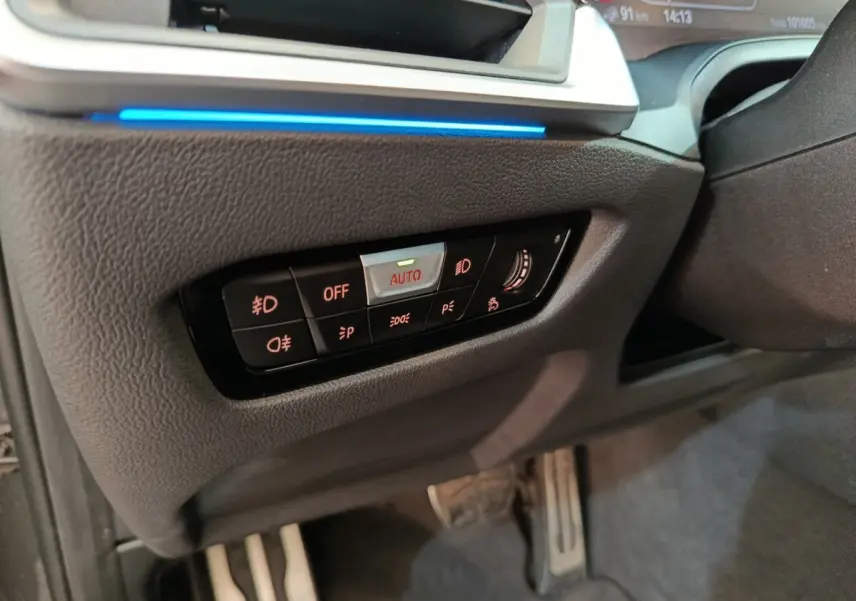 Détail du panneau de commandes d’éclairage avec bouton auto, sur le côté gauche du tableau de bord d’une BMW Série 3 gris foncé.