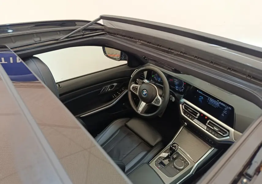 Vue intérieure côté conducteur d'une BMW Série 3 320e gris foncé, avec tableau de bord numérique et volant cuir multifonctions.