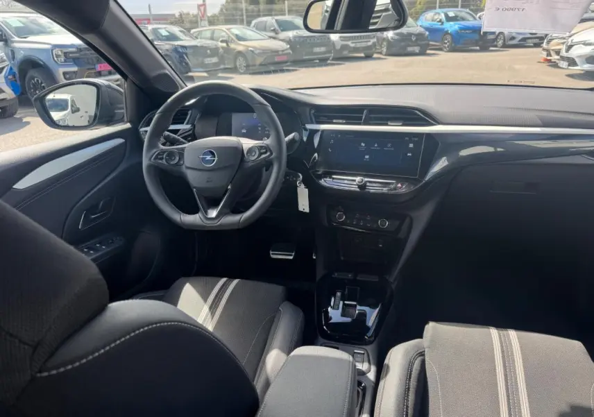 Vue intérieure avant de l’Opel Corsa 2025 noire, montrant le volant, la console centrale avec écran tactile et les sièges tissu à bandes claires.