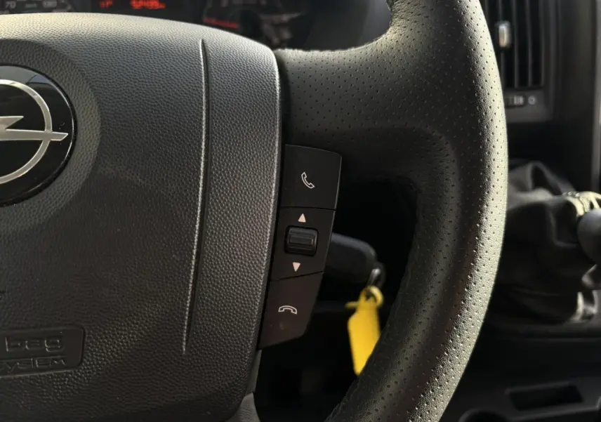 Gros plan sur le volant noir perforé d’un Opel Movano 2024 avec commandes téléphoniques et levier de vitesses manuel visible.