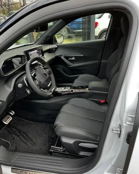 Vue intérieure côté conducteur du Peugeot 2008 blanc, mettant en valeur le tableau de bord numérique et les sièges en tissu noir.