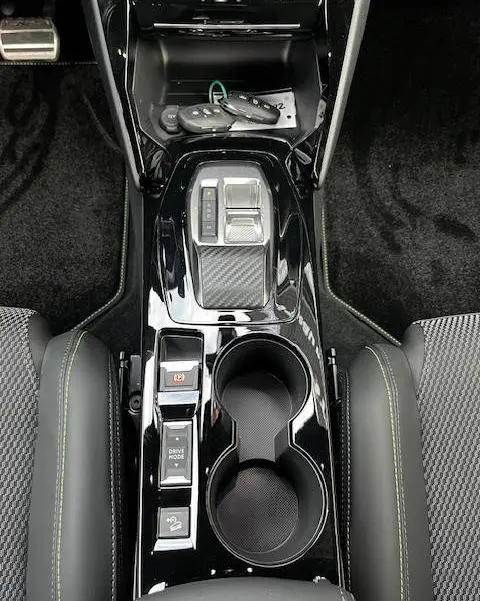 Vue plongeante sur la console centrale noire brillante du Peugeot 2008 GT 2024 avec commandes et porte-gobelets.