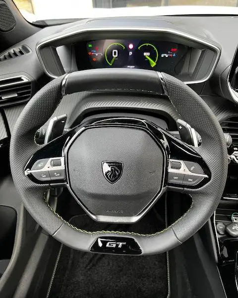 Vue rapprochée du volant GT noir avec surpiqûres vertes et tableau de bord numérique du Peugeot 2008 PureTech 130 2024.