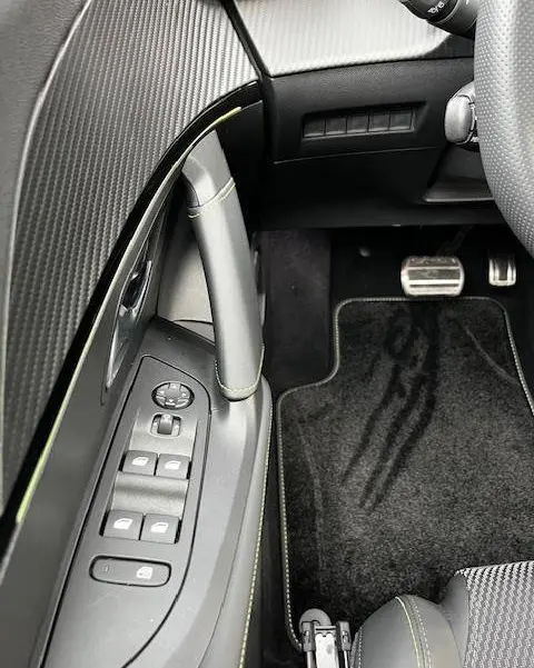 Vue intérieure côté gauche du Peugeot 2008 blanc 2024, mettant en valeur les commandes de vitres et le pédalier en aluminium.