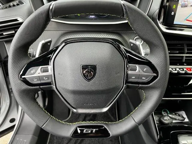 Vue rapprochée du volant cuir noir avec surpiqûres vertes et logo Peugeot au centre du Peugeot 2008 GT blanc 2024.