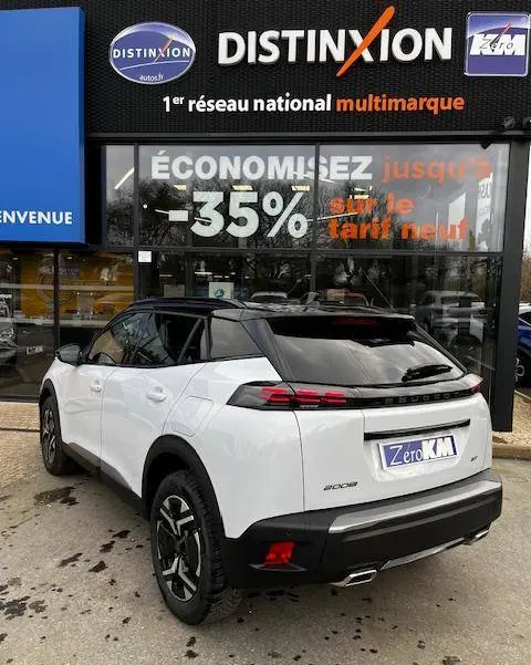 Vue 3/4 arrière droite d’un Peugeot 2008 blanc 2024 avec toit noir et feux arrière LED, devant une concession multimarque.