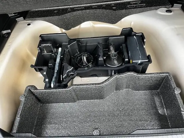 Vue plongeante sur le coffre blanc d'une Peugeot 2008 2024 avec rangement en mousse et kit de réparation intégré.