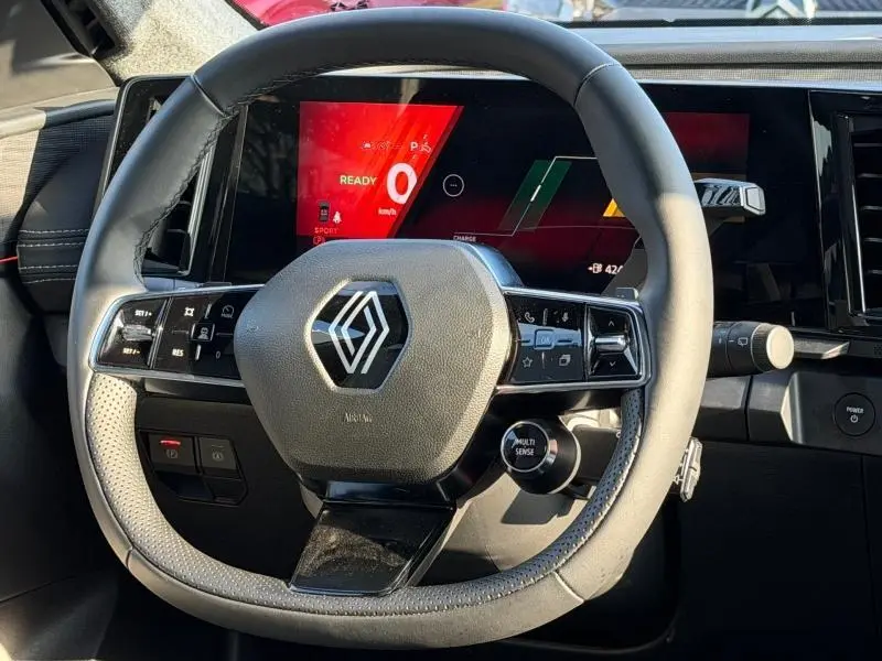 Vue rapprochée du volant gris clair de la Renault Scénic E-Tech 2025 avec écran numérique rouge et commandes multifonctions.