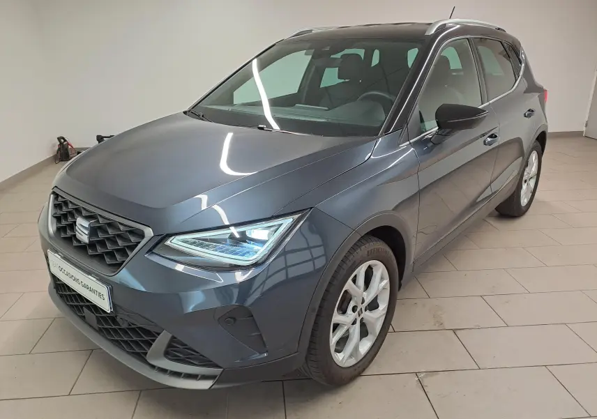 SEAT Arona 1.0 TSI 110 DSG7 FR gris magnétique avec toit noir, vue 3/4 avant droit en intérieur showroom.
