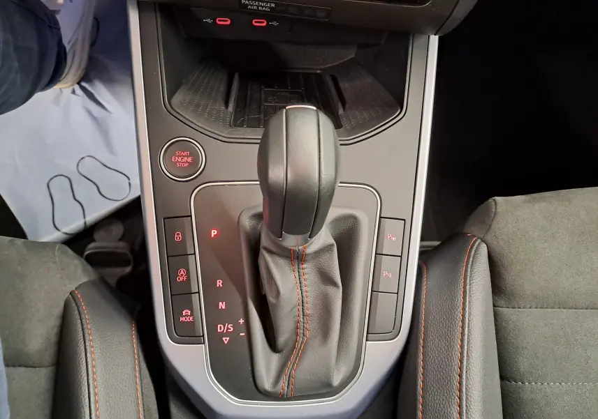 Vue rapprochée de la console centrale du SEAT Arona 2024, levier de vitesse automatique avec coutures orange et boutons lumineux.