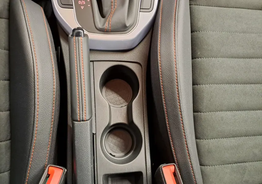 Vue plongeante sur la console centrale d'une SEAT Arona 2024, cuir noir avec surpiqûres orange et porte-gobelets.