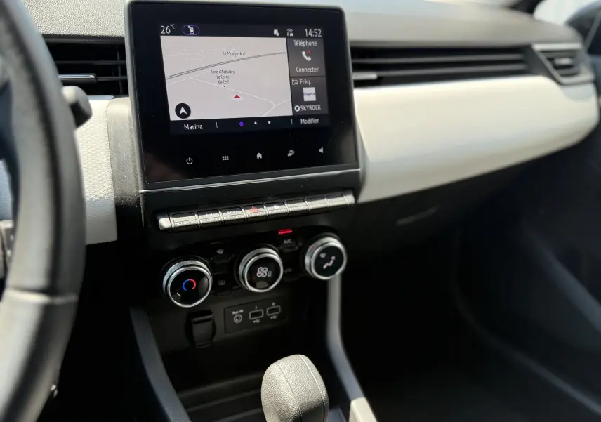 Vue intérieure centrée sur la console centrale de la Renault Clio V grise, avec écran tactile et commandes de climatisation.
