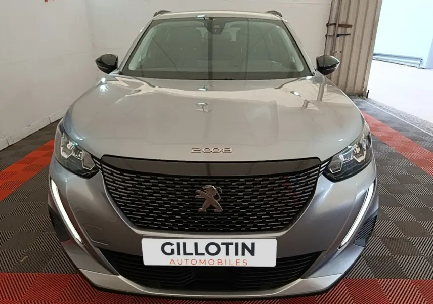 Vue avant d'un Peugeot 2008 gris clair avec calandre noire et feux LED en forme de griffes, dans un showroom.