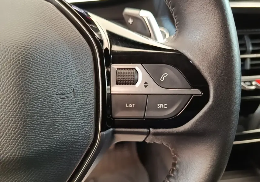 Gros plan sur les commandes gauche du volant cuir noir du Peugeot 2008, boutons de gestion audio et appel.