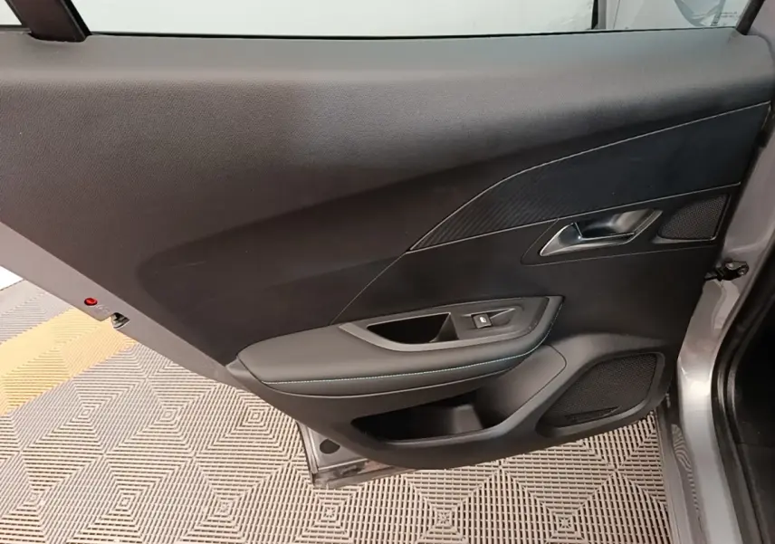 Porte intérieure côté gauche d’un Peugeot 2008 gris clair, avec garniture noire et surpiqûres bleues.
