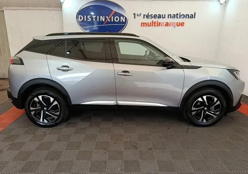 Profil côté gauche d’un Peugeot 2008 gris clair 2022 avec toit noir et jantes alliage bicolores, en intérieur showroom.