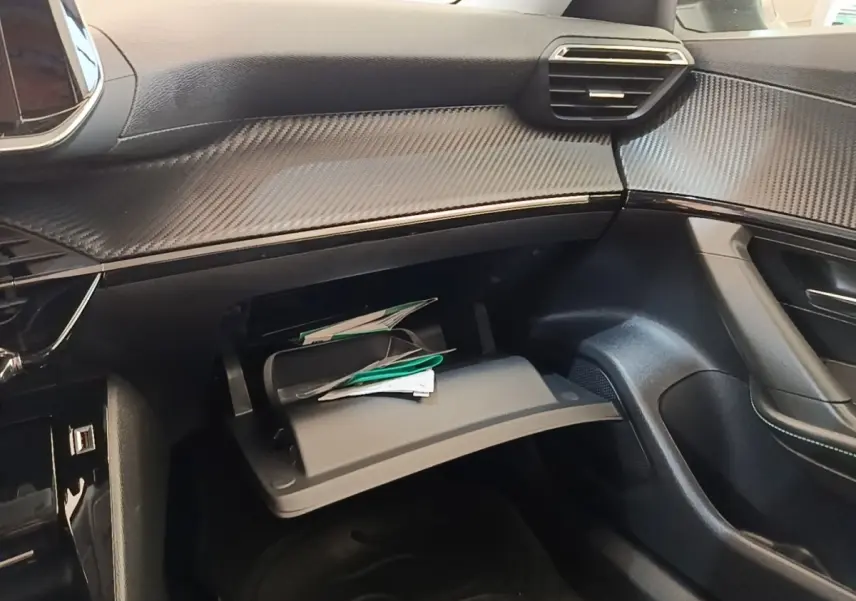 Vue intérieure côté passager du tableau de bord noir avec boîte à gants ouverte et finition effet carbone sur Peugeot 2008 gris clair.