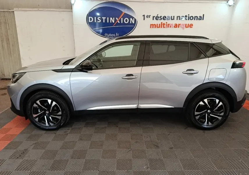 Vue latérale droite d’un Peugeot 2008 gris clair 2022 avec jantes noires et toit noir, en intérieur showroom.