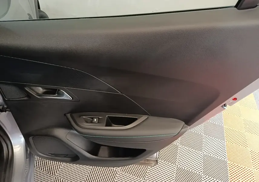 Vue intérieure du panneau de porte avant gauche gris clair du Peugeot 2008, avec commande de lève-vitre et poignée intégrée.