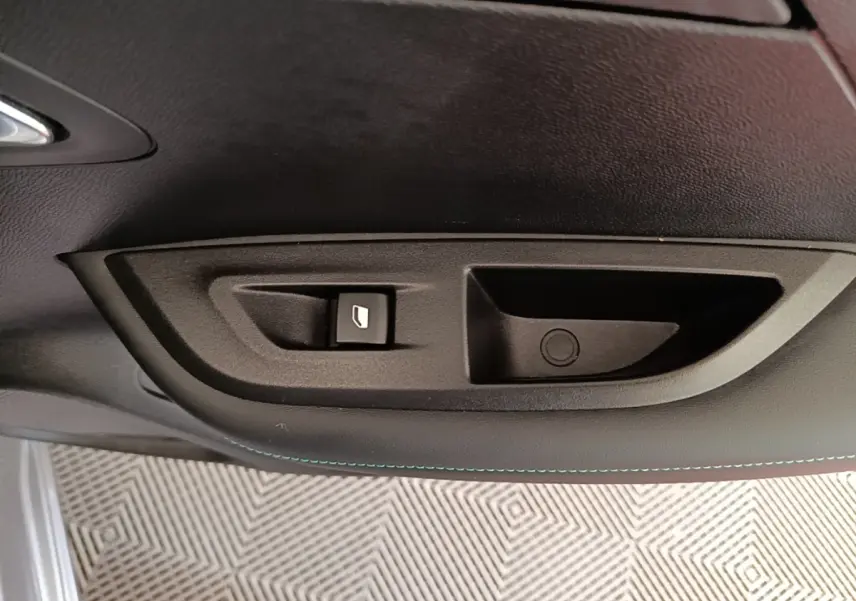 Détail de la commande de lève-vitre électrique sur la porte intérieure côté conducteur d’un Peugeot 2008 gris clair.