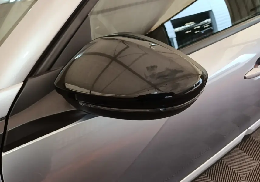 Gros plan sur le rétroviseur droit noir brillant du Peugeot 2008 gris clair, avec reflet de l'éclairage intérieur.