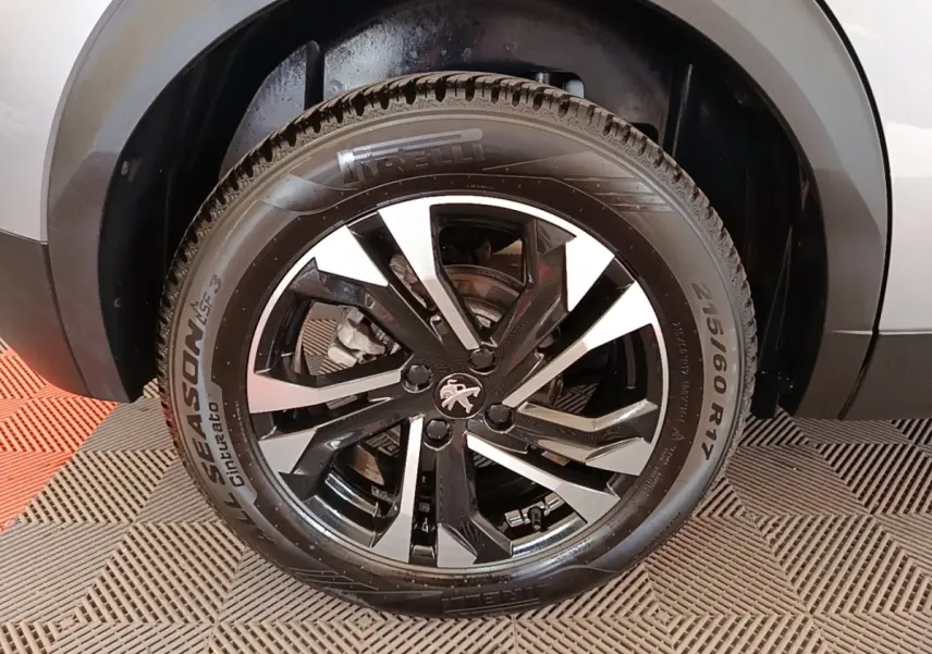 Gros plan sur la roue avant droite d’un Peugeot 2008 gris clair, jante alliage noir et argentée avec logo lion.