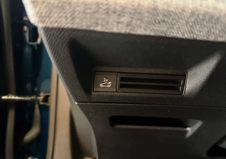 Détail intérieur montrant le bouton d'ouverture du hayon électrique sur la partie inférieure côté conducteur du Peugeot 3008 Bleu Obsession.