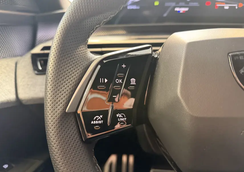 Gros plan sur les commandes à gauche du volant perforé du Peugeot 3008 Hybrid 145 GT, intérieur noir et gris.