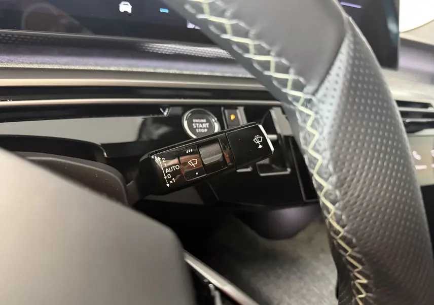 Gros plan sur la commande d’essuie-glace à gauche du volant perforé avec surpiqûres vert clair dans l’habitacle du Peugeot 3008 Hybrid 2025.