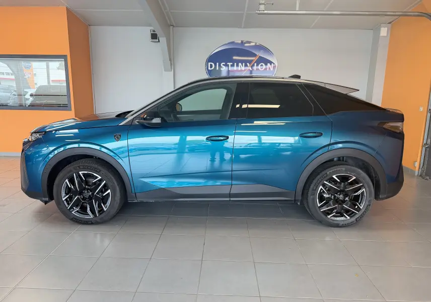 Vue de profil côté gauche du Peugeot 3008 Hybrid 145 GT bleu obsession avec toit noir et jantes alliage 19 pouces en intérieur showroom.