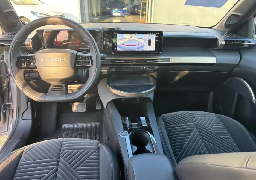 Vue intérieure avant de la Lancia Ypsilon 2025 gris, avec tableau de bord numérique et écran central affichant la caméra de recul.