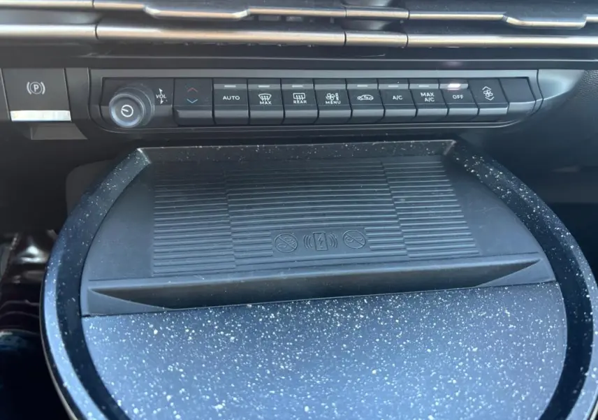 Vue rapprochée de la console centrale de la Lancia Ypsilon 2025, montrant les commandes de climatisation et un espace de rangement texturé gris.