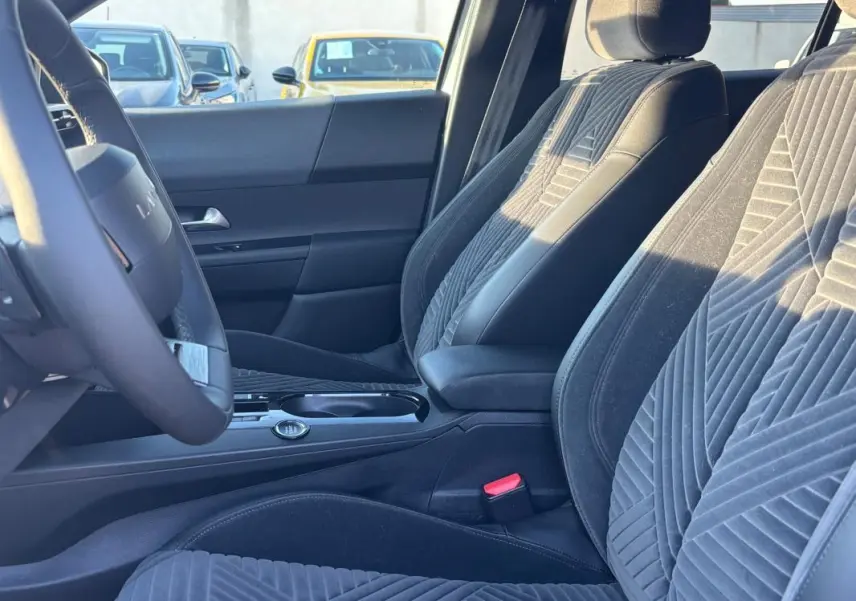 Vue intérieure côté conducteur de la Lancia Ypsilon 2025, montrant les sièges en tissu gris et le volant sport.