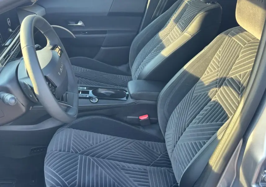 Intérieur avant droit de la Lancia Ypsilon gris 2025, sièges en tissu à motifs géométriques et volant sport visible.