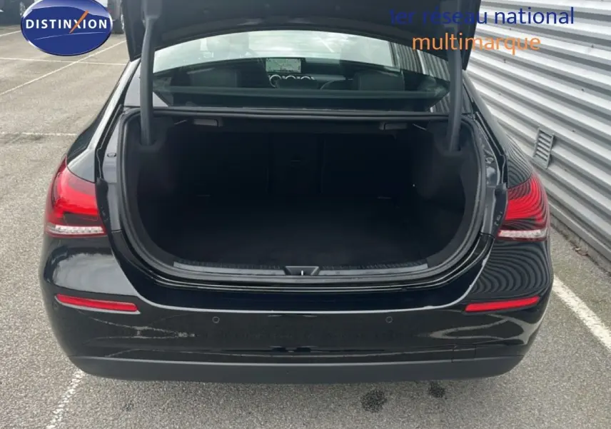 Vue arrière d'une Mercedes Classe A 180 Business Line noire Cosmos Metal avec coffre ouvert sur parking extérieur.