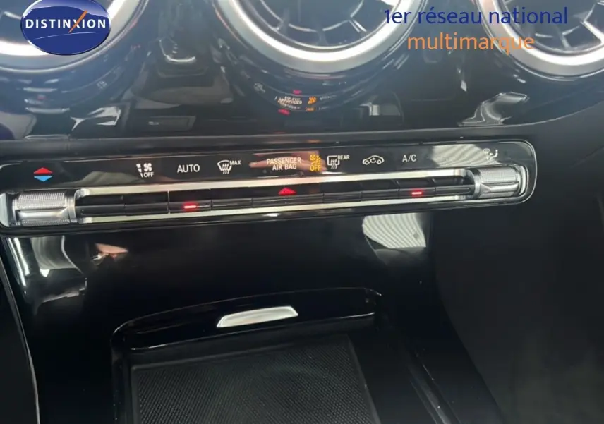 Gros plan sur la console centrale noire brillante de la Mercedes Classe A 180 Business Line avec commandes climatisation et aérateurs ronds.