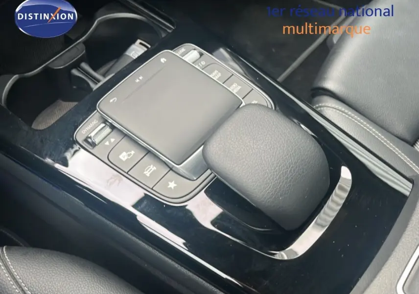 Gros plan sur la console centrale noire brillante de la Mercedes Classe A 180 Business Line avec pavé tactile et commandes intégrées.