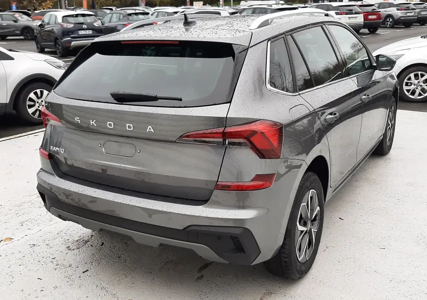 Vue 3/4 arrière droite d'un Skoda Kamiq gris graphite métallisé 2025 avec feux LED et toit avec barres de toit.