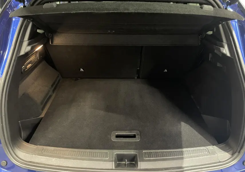 Coffre ouvert vu de l'arrière d'un Renault Austral 2024 bleu Iron, montrant l'espace de chargement vide et tapis noir.