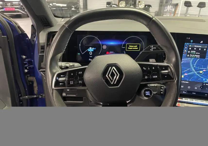 Vue intérieure centrée sur le volant noir avec logo Renault, tableau de bord numérique et écran tactile du Renault Austral Bleu Iron.