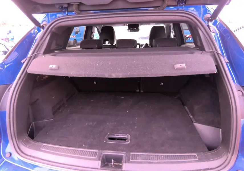 Vue arrière du coffre ouvert d'un Renault Austral 2024 en bleu Iron, montrant l'espace de chargement et la plage arrière.