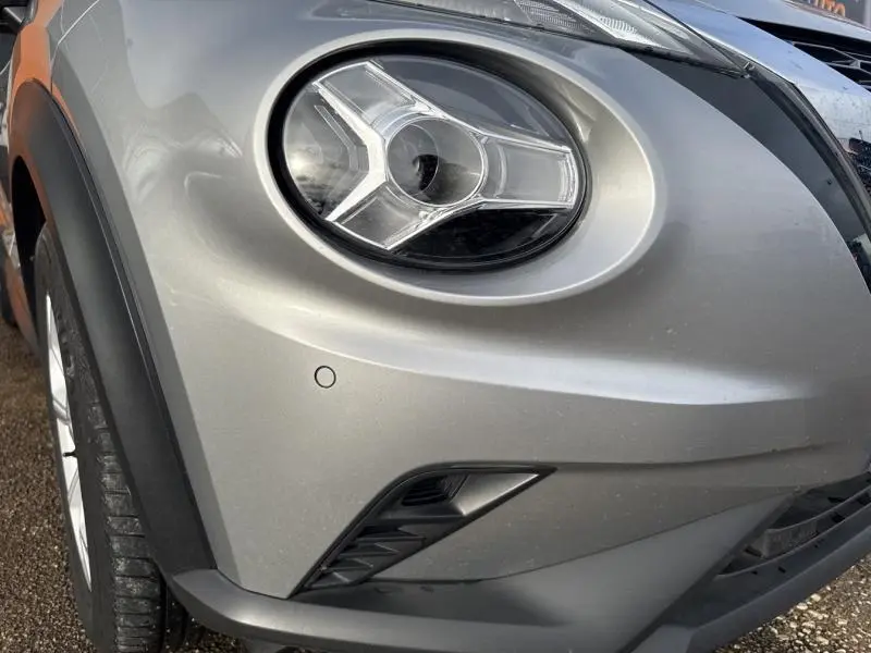 Gros plan sur le phare avant droit du Nissan Juke gris perle métallisé avec détails du pare-chocs et roue visible.