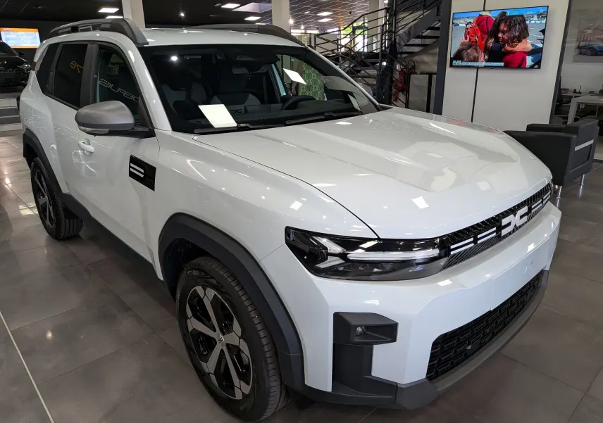 Vue 3/4 avant gauche d'un Dacia Bigster blanc glacier avec calandre noire et jantes bi-ton en showroom.