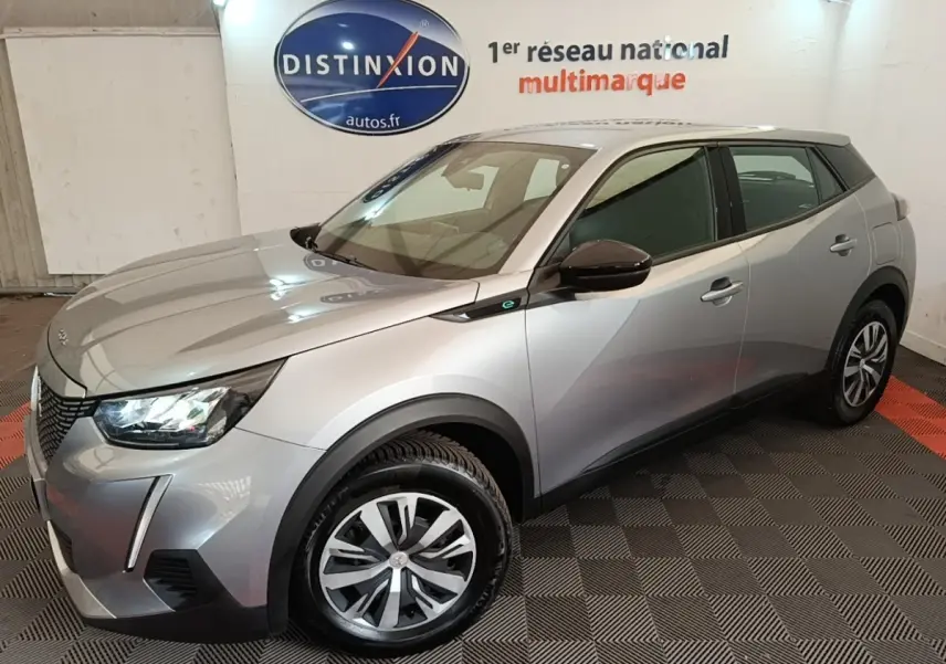 Peugeot E-2008 électrique gris clair en 3/4 avant droit, avec jantes spécifiques et rétroviseurs noirs brillants.