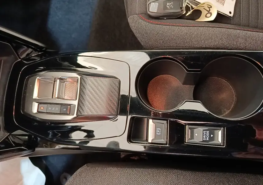 Vue rapprochée de la console centrale noire brillante du Peugeot E-2008 électrique avec sélecteur de vitesse et porte-gobelets.