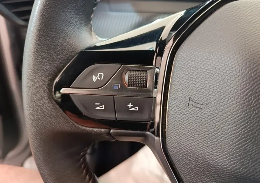 Gros plan sur le côté gauche du volant cuir multifonctions du Peugeot E-2008 électrique gris clair 2023.