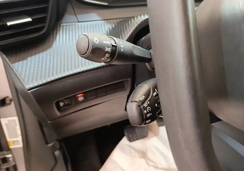 Gros plan sur la colonne de direction et commandes derrière volant cuir noir du Peugeot E-2008 électrique gris clair.